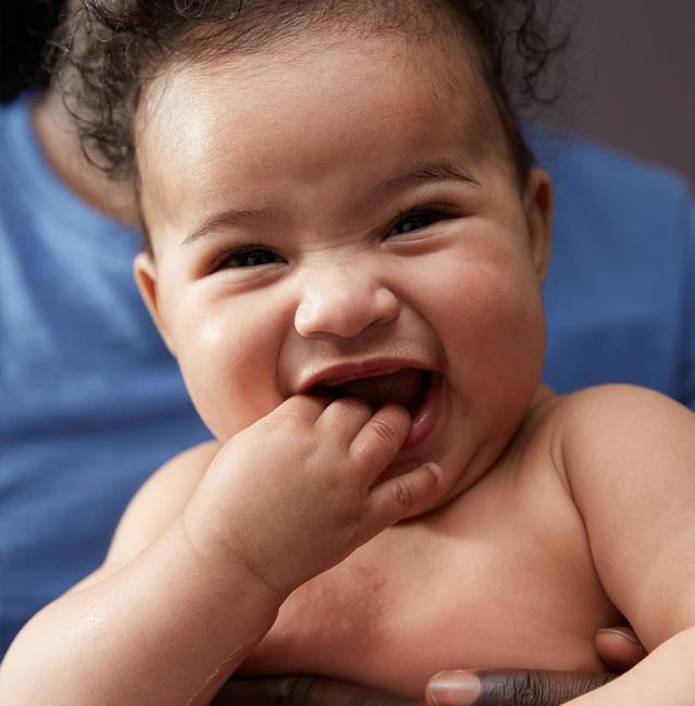 Bebê sorrindo com a mão na boca